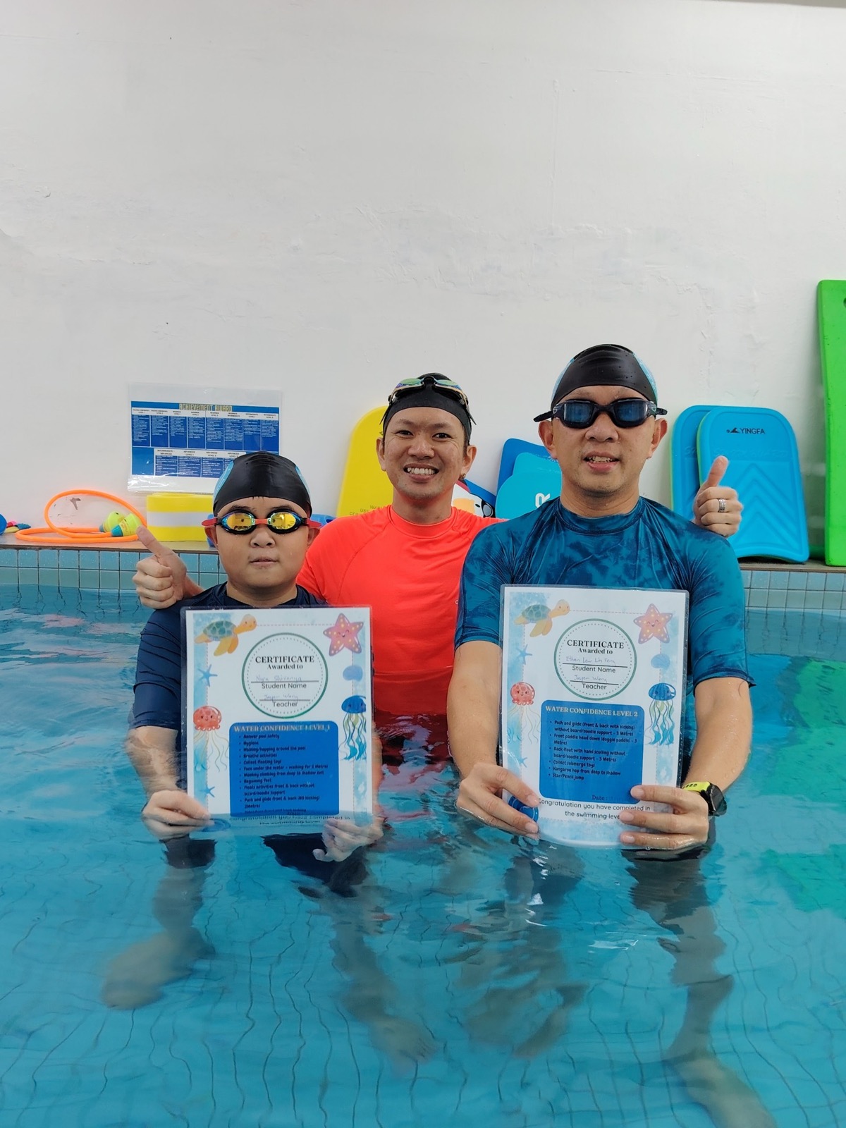 Coach Jasper celebrating with a young swimmer and an adult learner holding their Water Confidence certificates